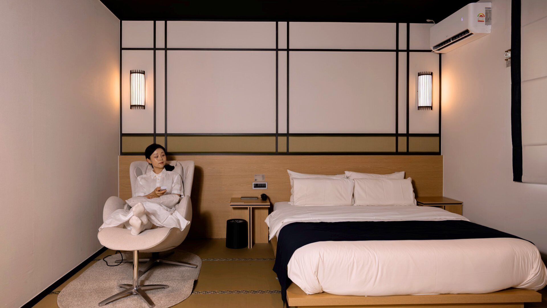A hotel room with a bed, a chair, bedside tables, and wall-mounted lights.