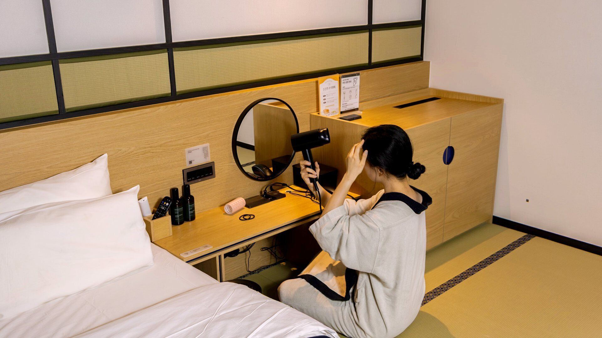 A hotel room with a bed, a wooden desk with a mirror, a hairdryer, and a small box.
