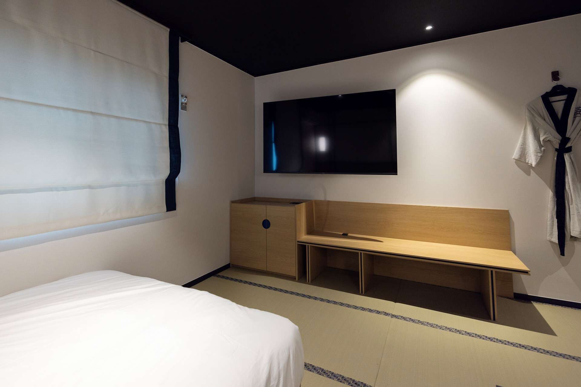 Una habitación de hotel con cama, un banco de madera, un televisor de pantalla plana y un perchero.