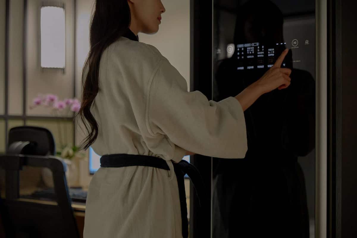 A person in a white robe standing in front of a glass door with a control panel.