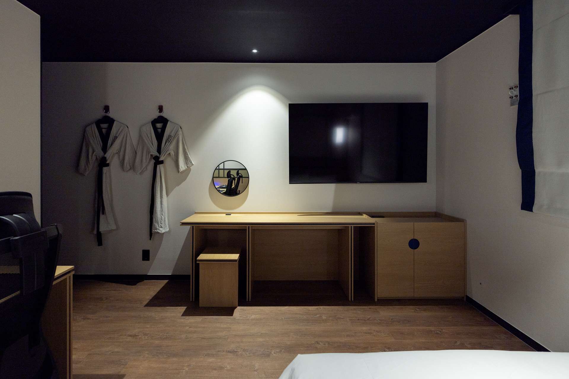 A modern bedroom with a wooden desk, a bed, and a TV mounted on the wall.