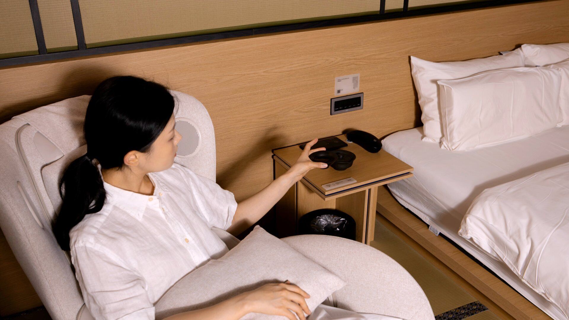 A hotel room with a bed, a bedside table with a phone and a remote control, and a wall-mounted air purifier.