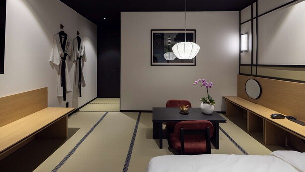 A modern hotel room with a tatami mat floor, a wooden bench, a dining table with a vase of flowers, a red chair, a bed, and a large mirror. - Mitasuya Ryokan Hotel by Anook Daejeon Yuseong (Daejeon)