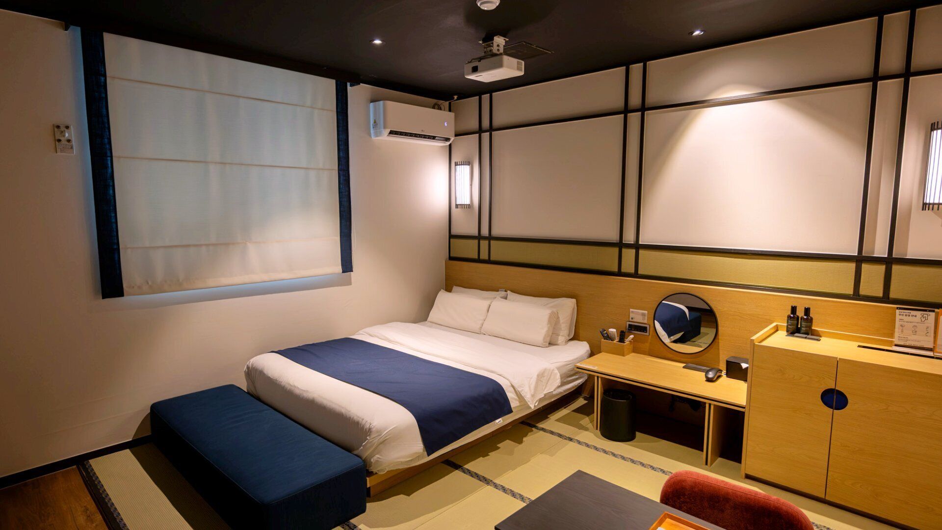 Una habitación de hotel con cama, mesita de noche, escritorio, silla y un armario pequeño.