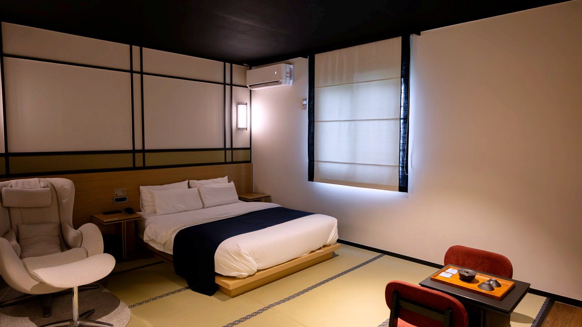 A hotel room with a bed, a chair, a small table, and a window.