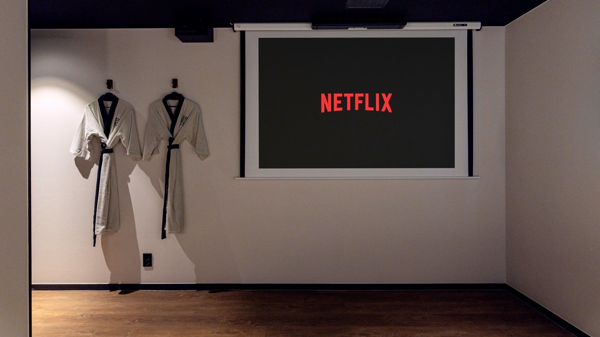 A room with a projector screen displaying 'NETFLIX' and two robes hanging on the wall.