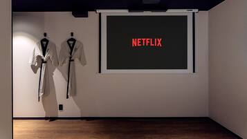 A room with a projector screen displaying 'NETFLIX' and two robes hanging on the wall.