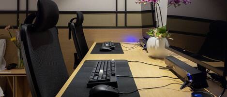 A workspace with a desk, computer, keyboard, mouse, and monitor. There are two chairs, a vase with flowers, and a plant on the desk.