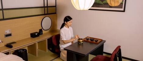 A hotel room with a bed, a desk with a computer, a chair, a small table with a tea set, and a wall-mounted mirror.
