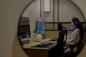 Une personne est assise à un bureau devant un ordinateur, avec un casque et un clavier. Un vase rempli de fleurs est posé sur le bureau.