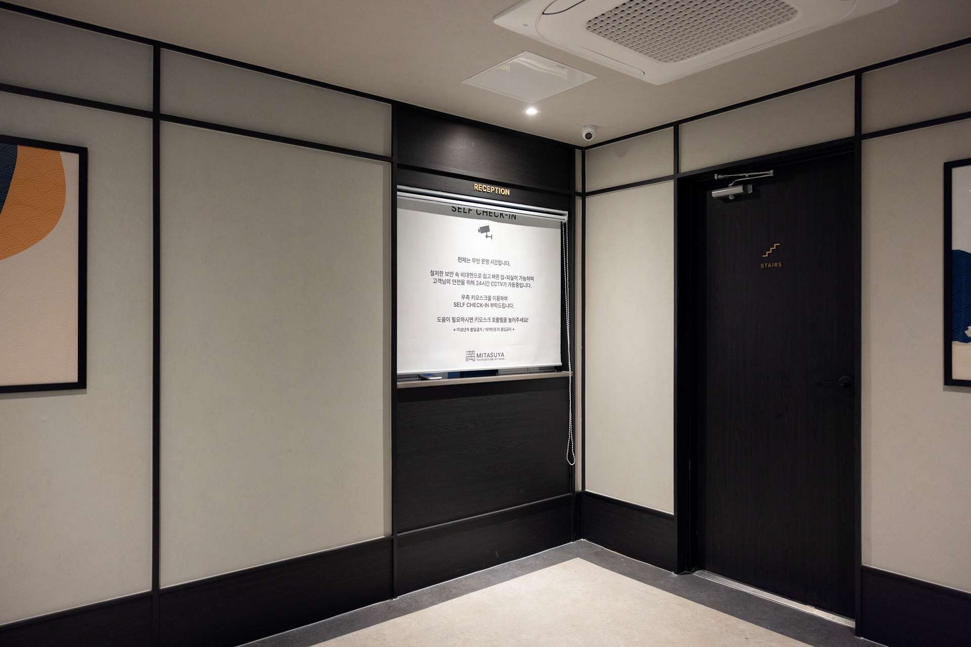 A reception area with a reception desk, a sign indicating self check-in, and a door labeled 'STAIRS'.