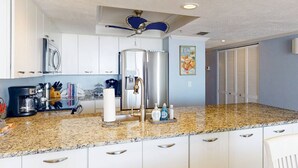 Een moderne keuken met witte kasten, een granieten aanrechtblad, roestvrijstalen apparatuur en een plafondventilator.