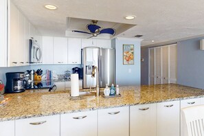 A modern kitchen with white cabinets, a granite countertop, stainless steel appliances, and a ceiling fan.
