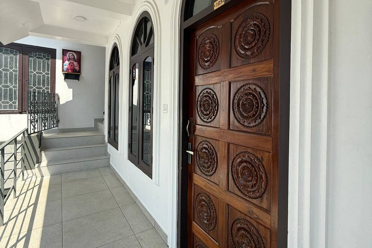 A building entrance with a wooden door, a staircase, and a small outdoor area with a metal railing.