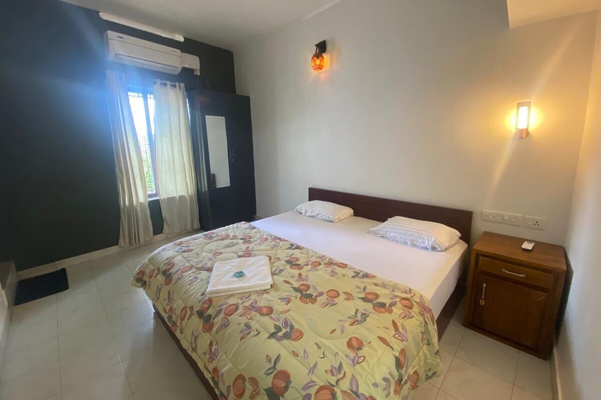 A hotel room with a large bed, a bedside table, a wall-mounted light, and a window with curtains.