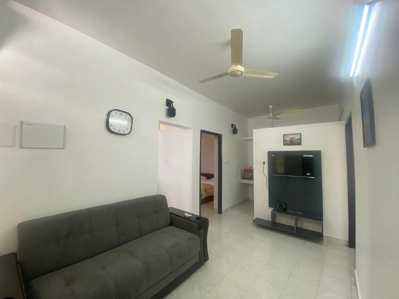 Un salon comprenant un canapé, un ventilateur de plafond, un téléviseur et une porte donnant sur une autre pièce.