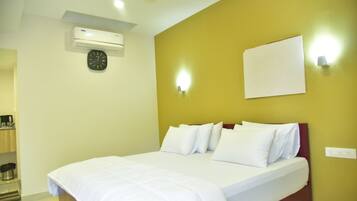 A hotel room with a bed, a wall clock, an air conditioning unit, and a light switch.