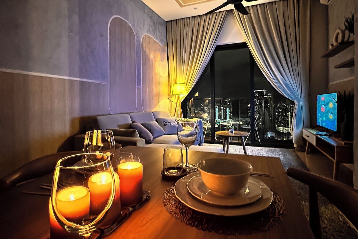 Une chambre d’hôtel moderne avec vue sur la ville, un coin repas éclairé à la bougie et un ventilateur de plafond.
