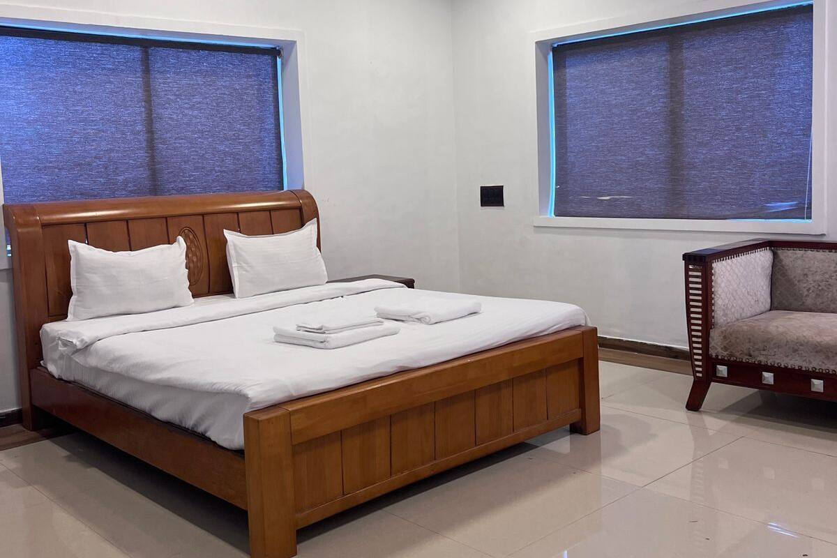 A bedroom with a wooden bed, two windows with blue curtains, a ceiling fan, and a small chair.