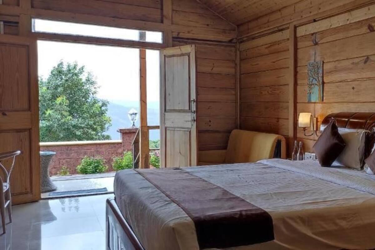 A wooden cabin bedroom with a bed, a chair, and a view of greenery outside.