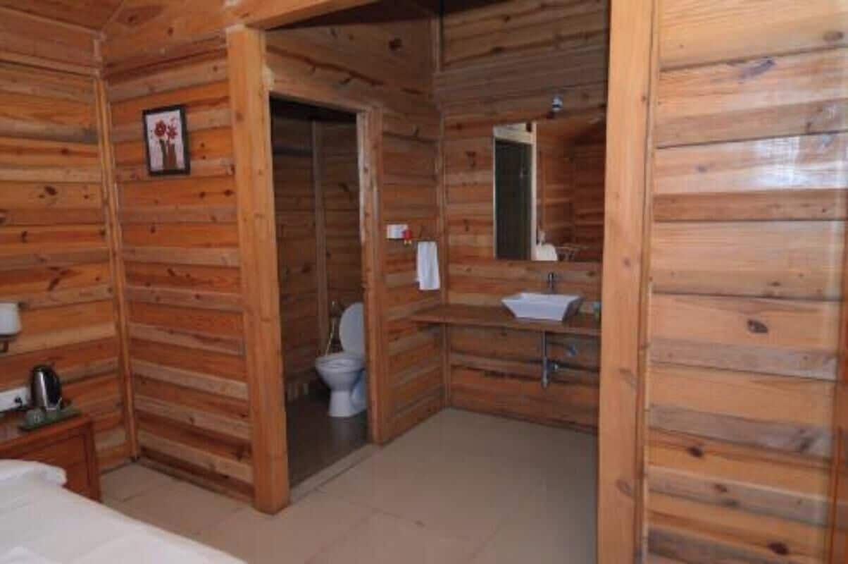 Una habitación de cabaña de madera con una cama, una mesita con un hervidor de agua, y un baño con inodoro y lavamanos.
