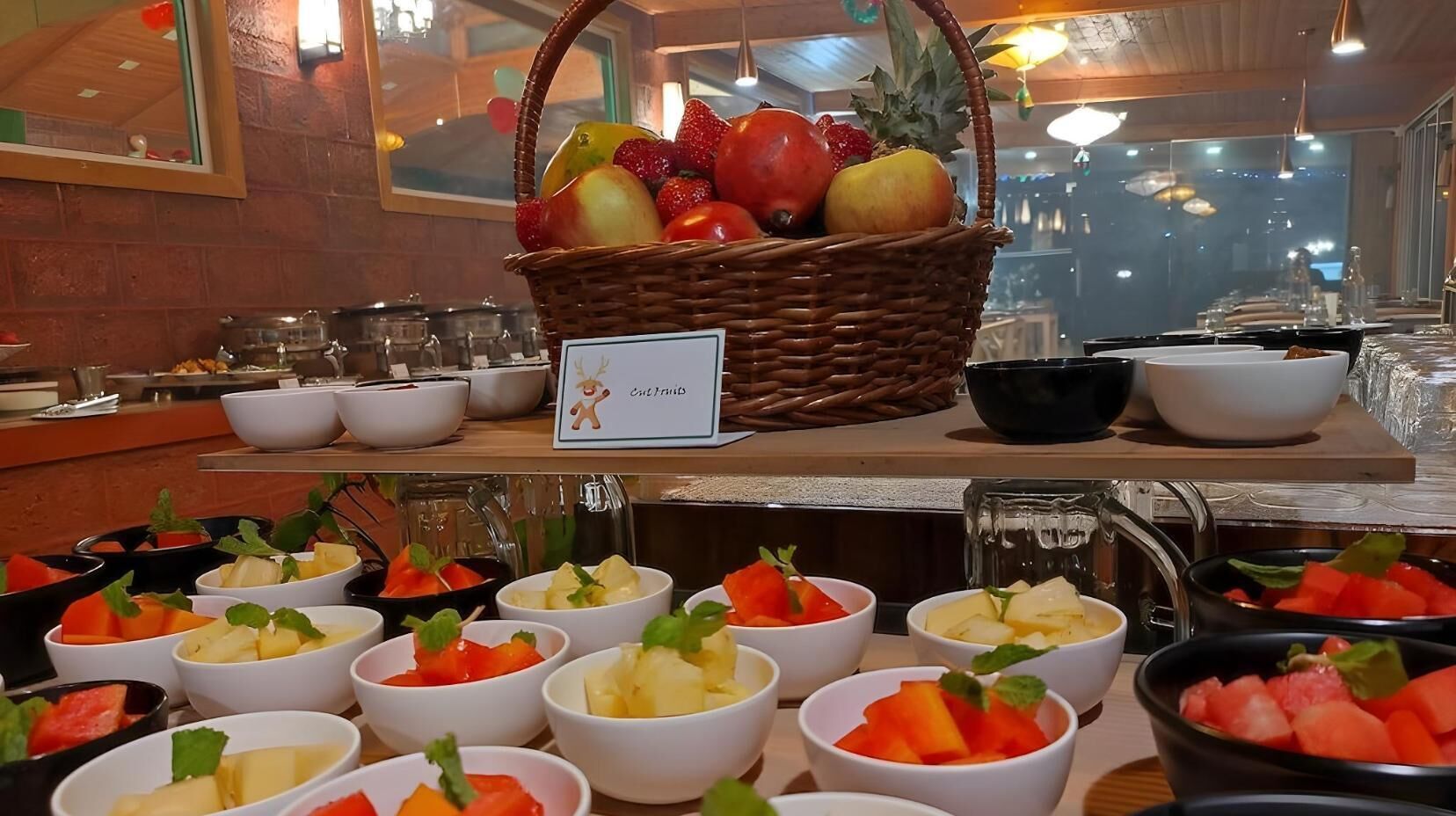 A buffet with various fruit bowls and a wicker basket filled with fruits.