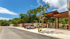 A modern building with a covered outdoor area, a paved driveway, and parked cars. - Chic and cozy 1-bedroom apartment with fuil bad,  AC ,TV and free WIFI (Tulum)