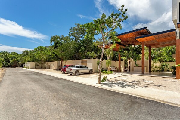 A modern building with a covered outdoor area, a paved driveway, and parked cars.