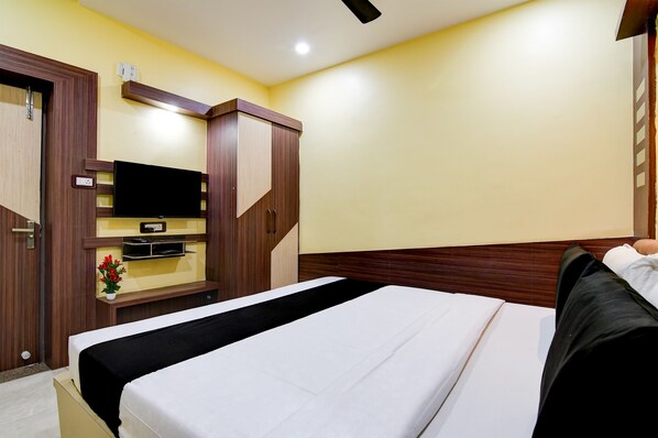 A hotel room with a bed, wooden wardrobe, TV, and a small table with a flower vase.