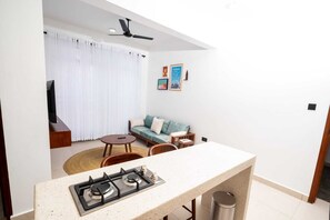 Eine kleine Küche mit einem Gasherd, ein Essbereich mit rundem Tisch und Stühlen, eine Couch und ein Deckenventilator.
