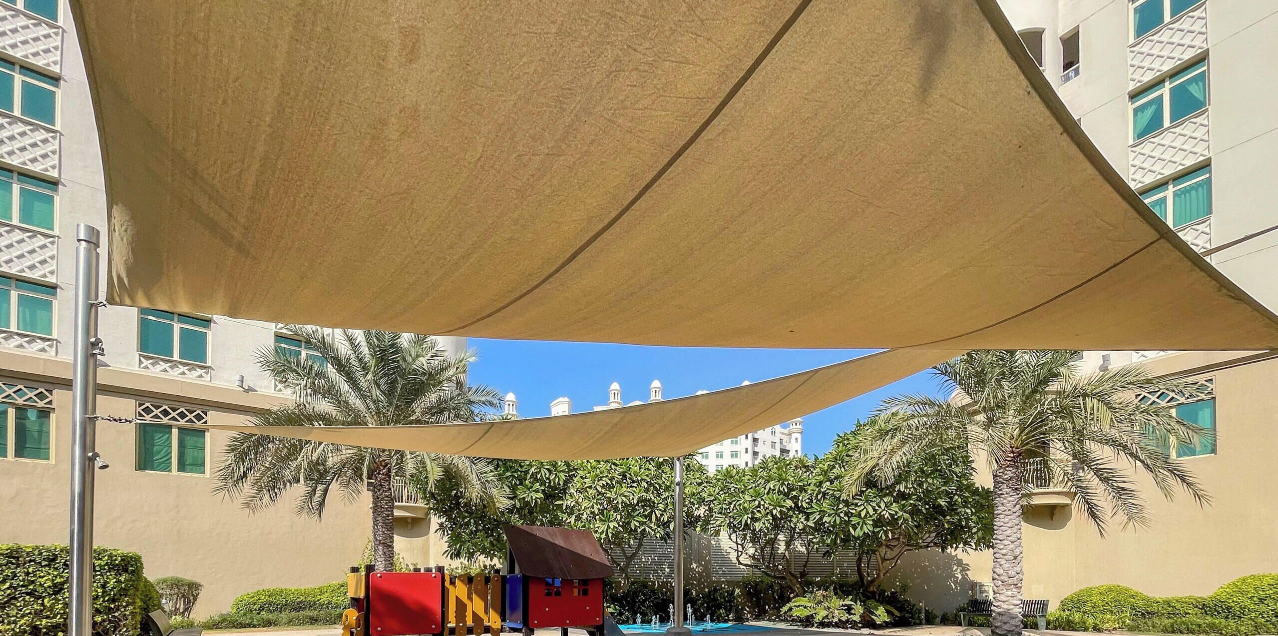 Zona de juegos con un sube y baja, una estructura para escalar y una zona sombreada.