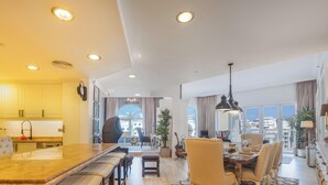 Un espacio habitable amplio con una gran mesa de comedor de madera, una cocina con armarios blancos y vistas a la ciudad a través de grandes ventanales.