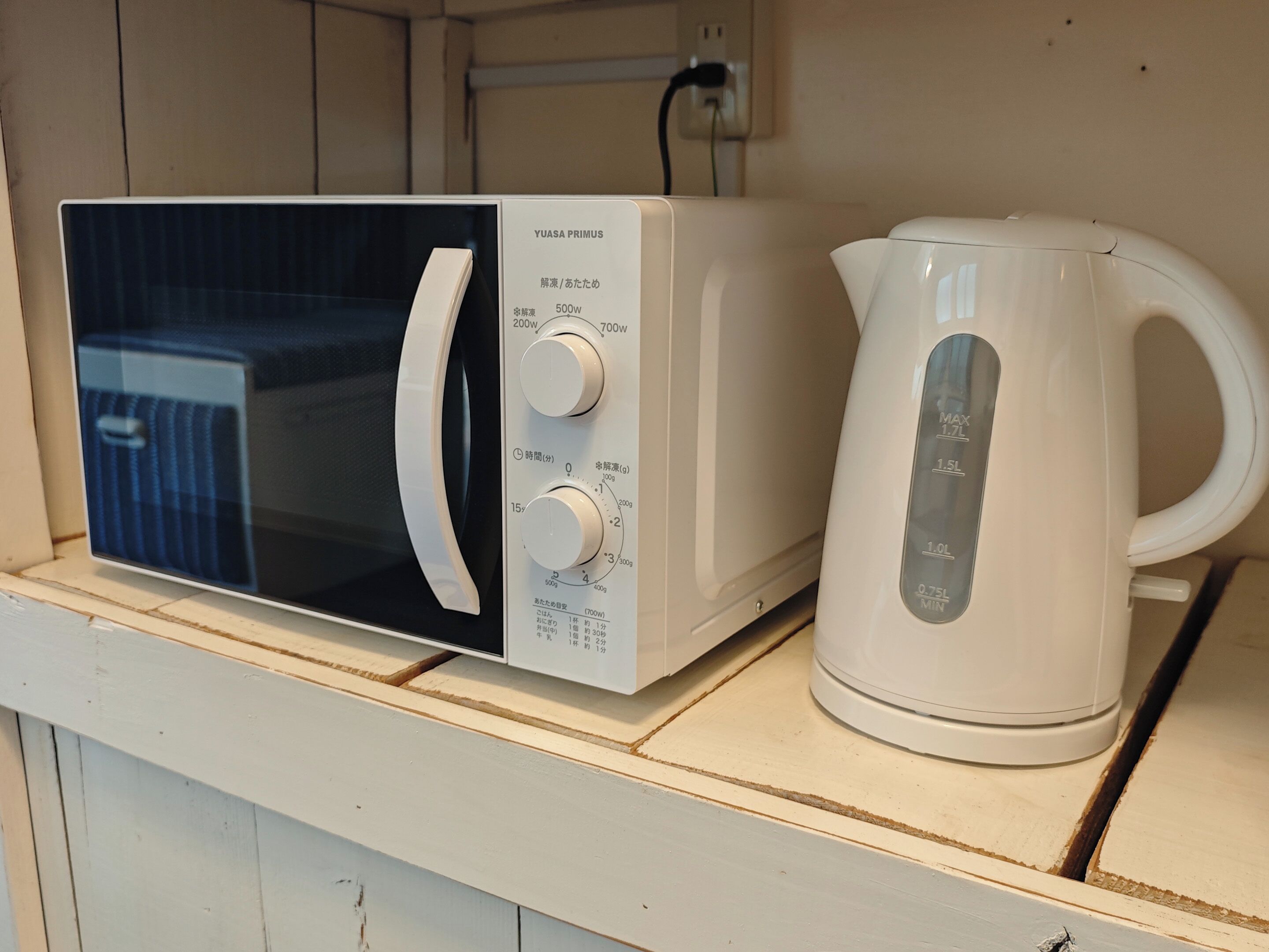 Un microondas y una tetera eléctrica blanca sobre una repisa de madera.
