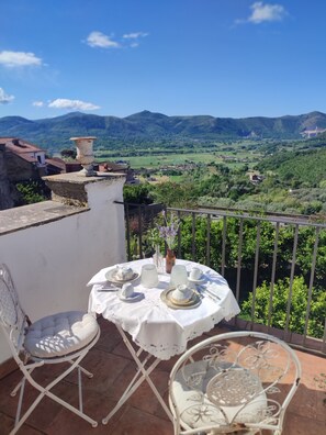 A round table set for two with white tablecloth and plates, a vase with flowers, and a view of green hills and mountains in the background. - A historic home with a superb view of the hills, just 20" from the Royal Palace of Caserta. (Caiazzo)