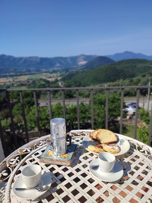 A table with a mug, a cup, a plate with food, and a thermos on a balcony overlooking a scenic landscape. - A historic home with a superb view of the hills, just 20" from the Royal Palace of Caserta. (Caiazzo)