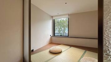 A minimalist room with tatami mats, a window with a view of trees, and a low ceiling.