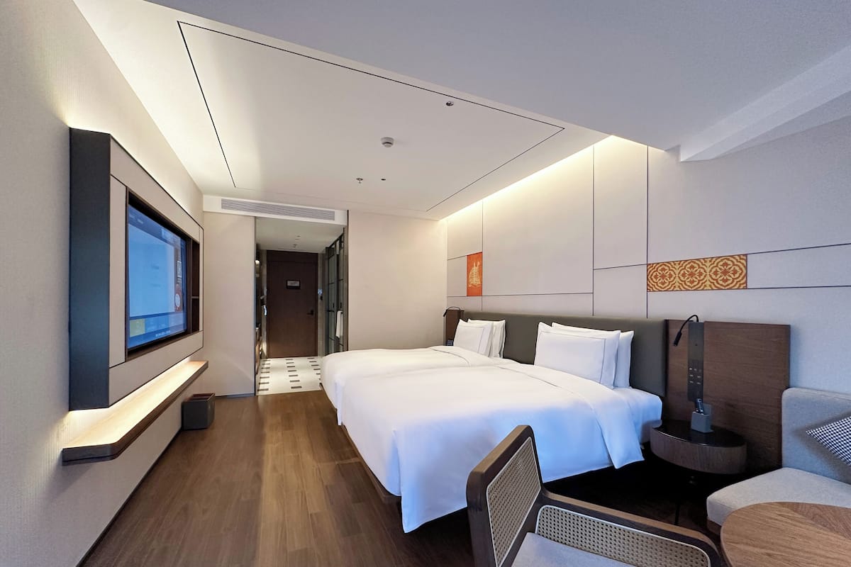 Une chambre d’hôtel moderne avec un grand lit, un bureau et un téléviseur fixé au mur.