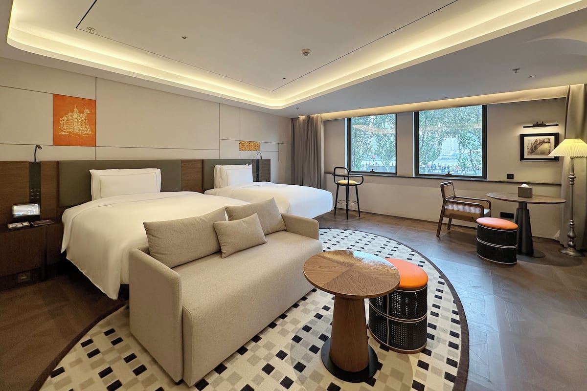 Une chambre d’hôtel moderne, dotée d’un grand lit, d’un canapé, d’un bureau et d’une chaise. Les fenêtres offrent une vue sur la ville.