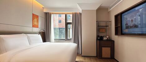 A hotel room with a large bed, a television mounted on the wall, and a window with a view of buildings outside.