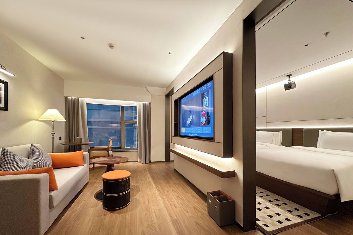 Une chambre d’hôtel avec un lit, un canapé, un téléviseur fixé au mur, une petite table et une fenêtre avec des rideaux.