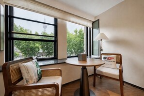 A room with a round table, two chairs, a lamp, and a view of trees and a tower through large windows. - UrCove by Hyatt Shanghai on the Bund (Shanghai)