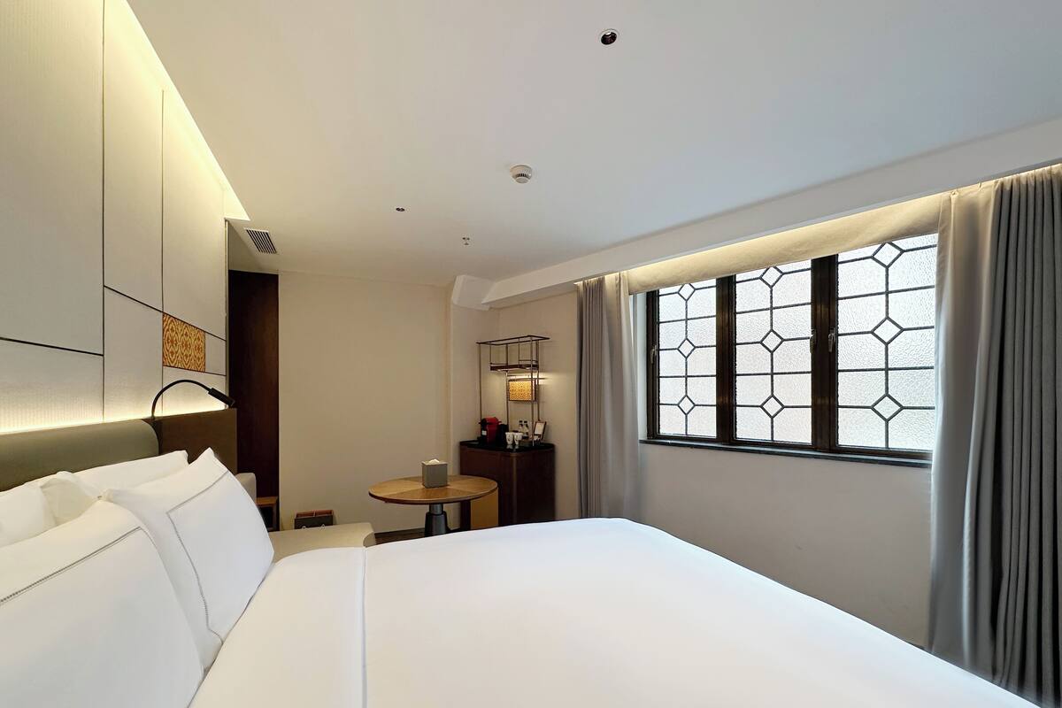 Une chambre d’hôtel avec un grand lit, une table de chevet, une petite table ronde et une fenêtre avec des rideaux.