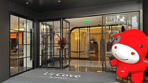Ein Hotel Eingang mit einer großen roten Maskotte, Glastüren und einem Schild mit der Aufschrift 'Ur Cove by Hyatt'.