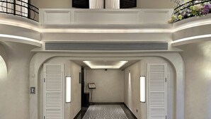 Eine moderne Hotelhalle mit Marmorboden, zwei Türen, einem gemusterten Teppich und einem Balkon mit Blumen.