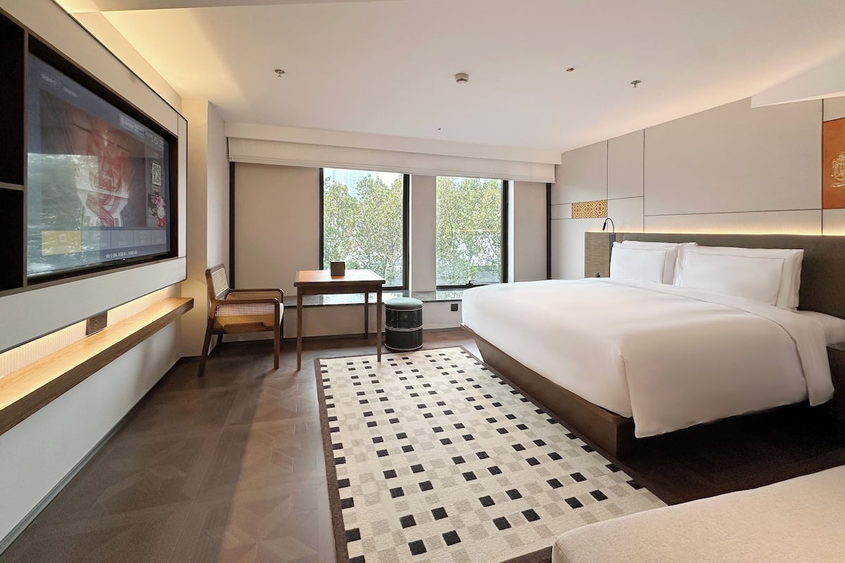 Une chambre d’hôtel moderne, dotée d’un grand lit, d’un bureau et d’un téléviseur fixé au mur.