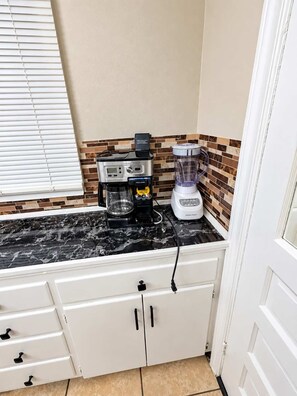 A kitchen with a coffee maker, a blender, and a tiled backsplash.
