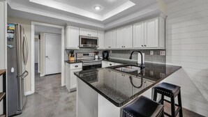 Una cocina moderna con armarios blancos, un refrigerador de acero inoxidable, un microondas y una isla grande con encimera negra.