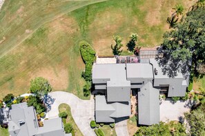 An aerial view of a residential property with a large house, a driveway, and surrounding greenery.