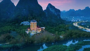 A hotel with a central tower and multiple rooms, surrounded by lush greenery and a river. - Yangshuo Norton Manor Resort (Guilin)