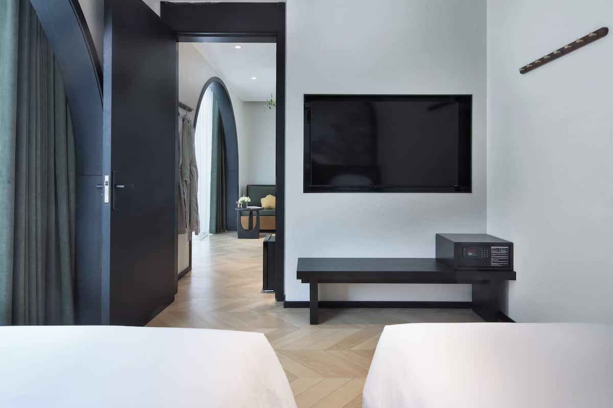 A modern hotel room with a large flat-screen TV mounted on the wall, a bench, and two beds.